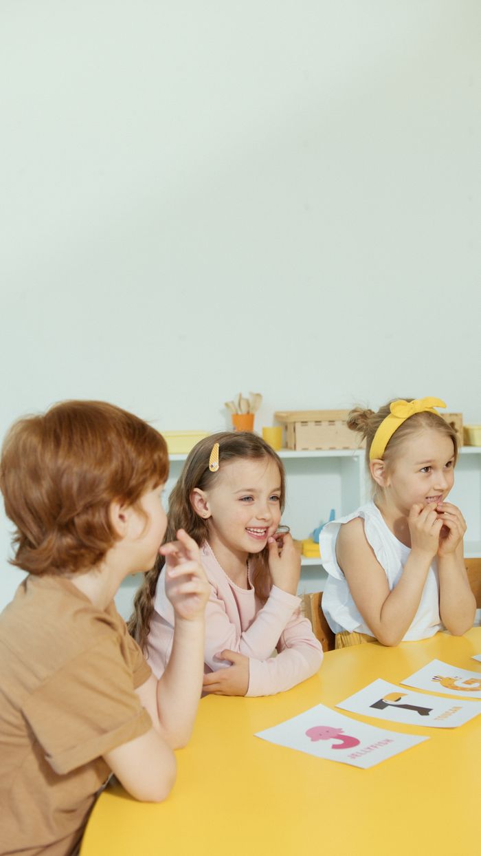 Group of children laughing and participating in a classroom setting around a yellow table.